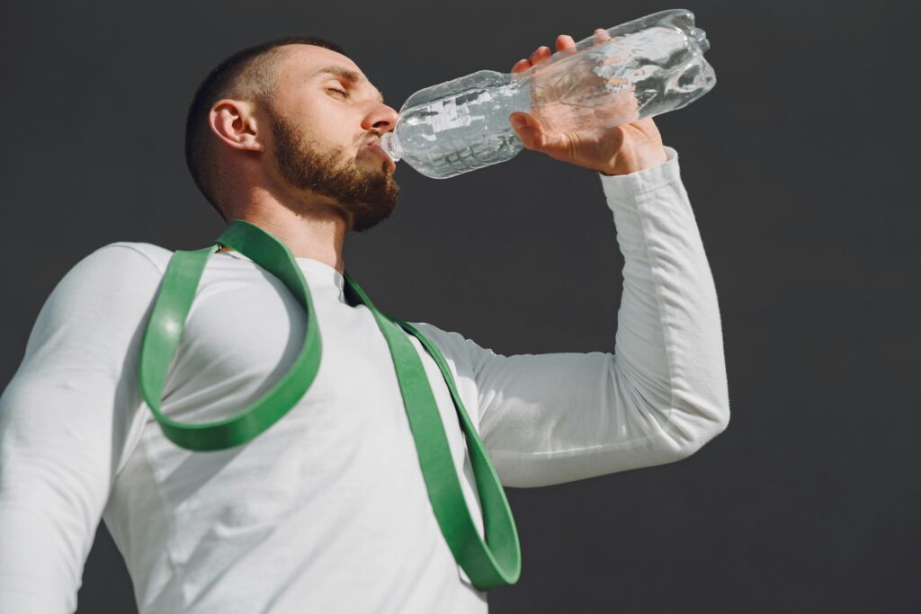 A fit man in sportswear drinking water outdoors, highlighting hydration and fitness.