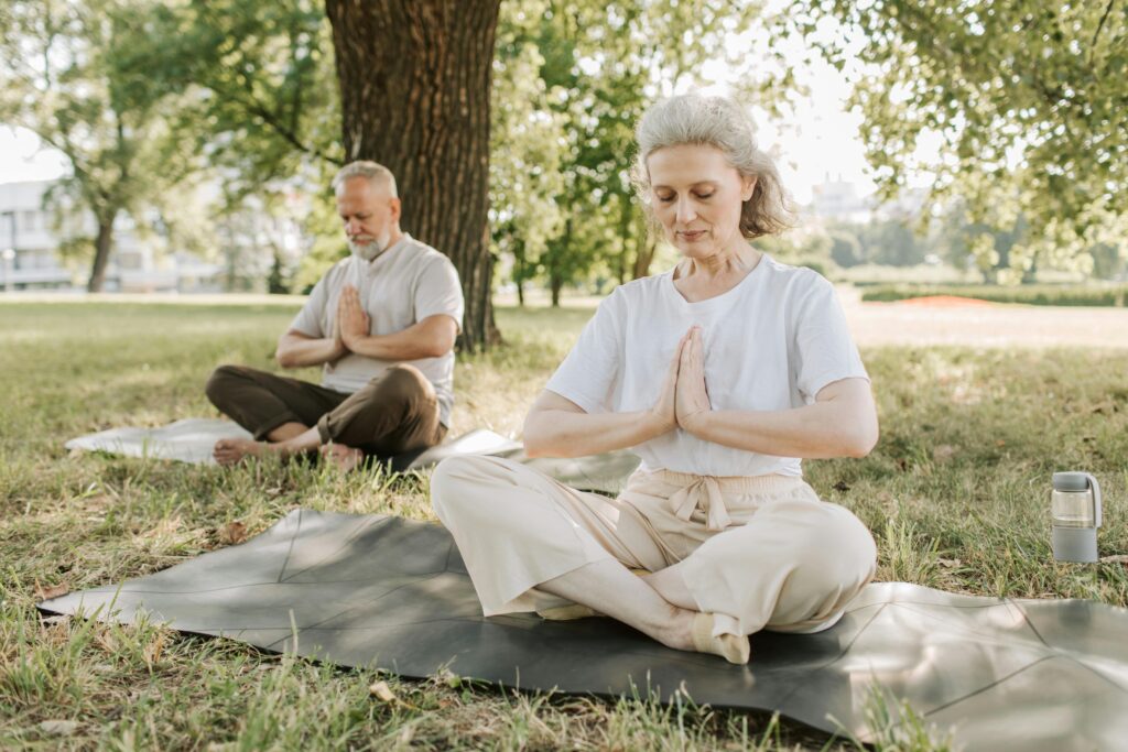 Elderly couple practicing yoga meditation outdoors, focusing on health and tranquility.