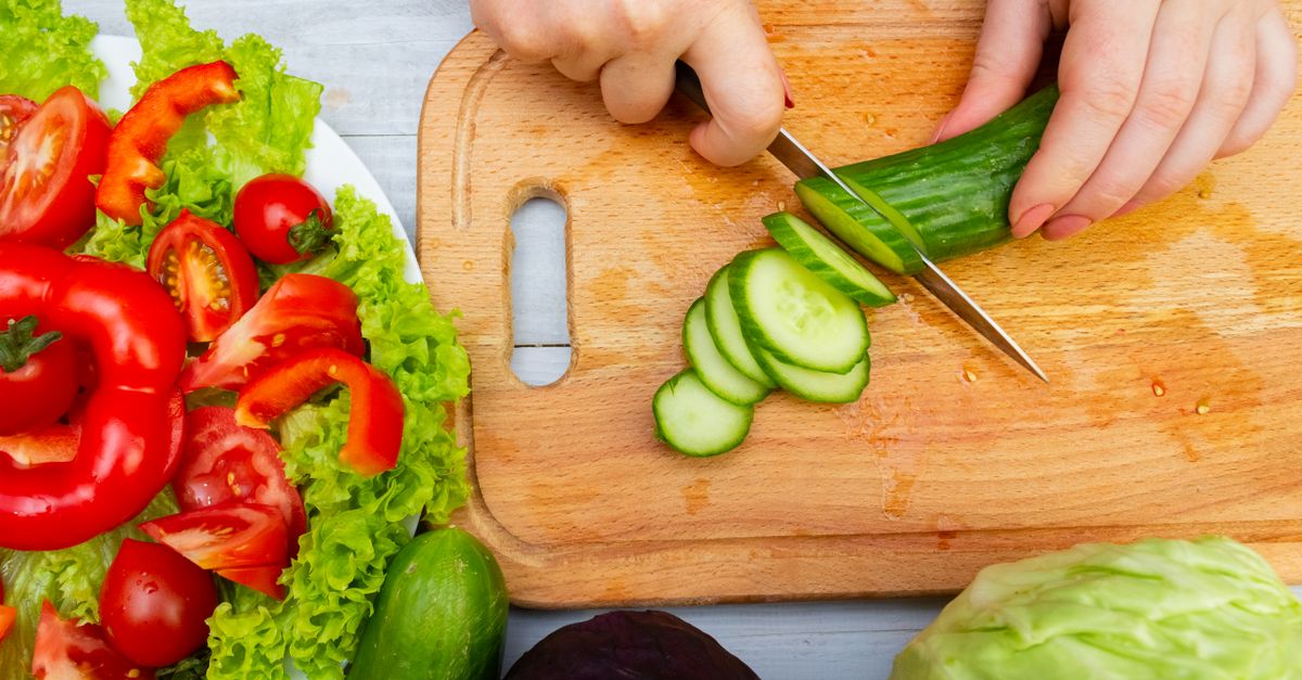 Fresh vegetables being sliced on a cutting board for a healthy meal prep.