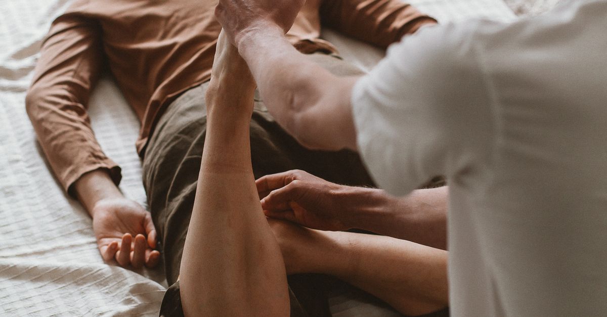 Therapist helps client stretch during a physiotherapy session indoors.