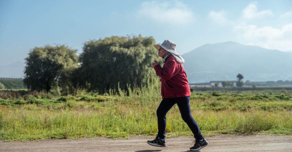 A woman in sportswear jogs along a rural road, surrounded by lush countryside and mountains.