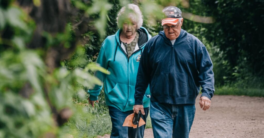 An elderly couple strolling with their pet dog in a scenic green park on a pleasant day.