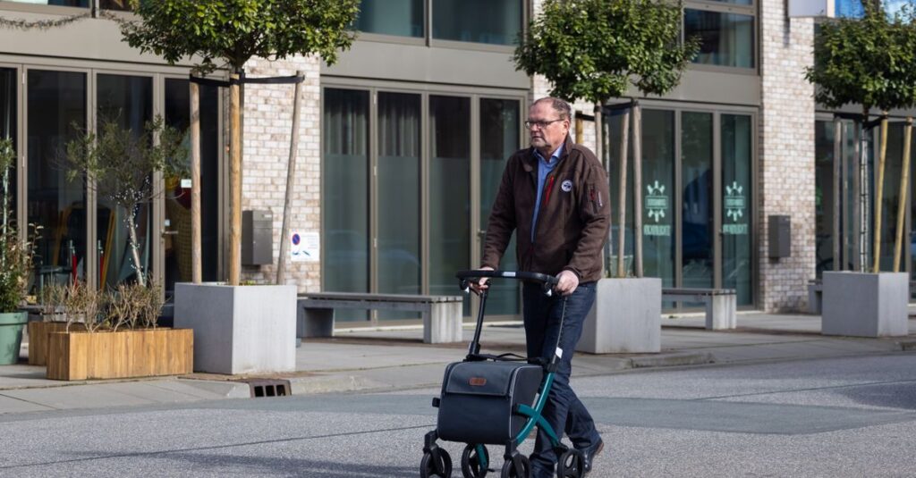 Senior man using a rollator while walking on a city street, showcasing urban mobility.
