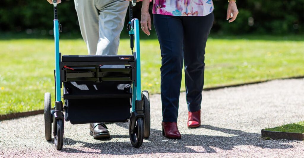 Elderly couple walking together with a walker on a sunny day in a park.