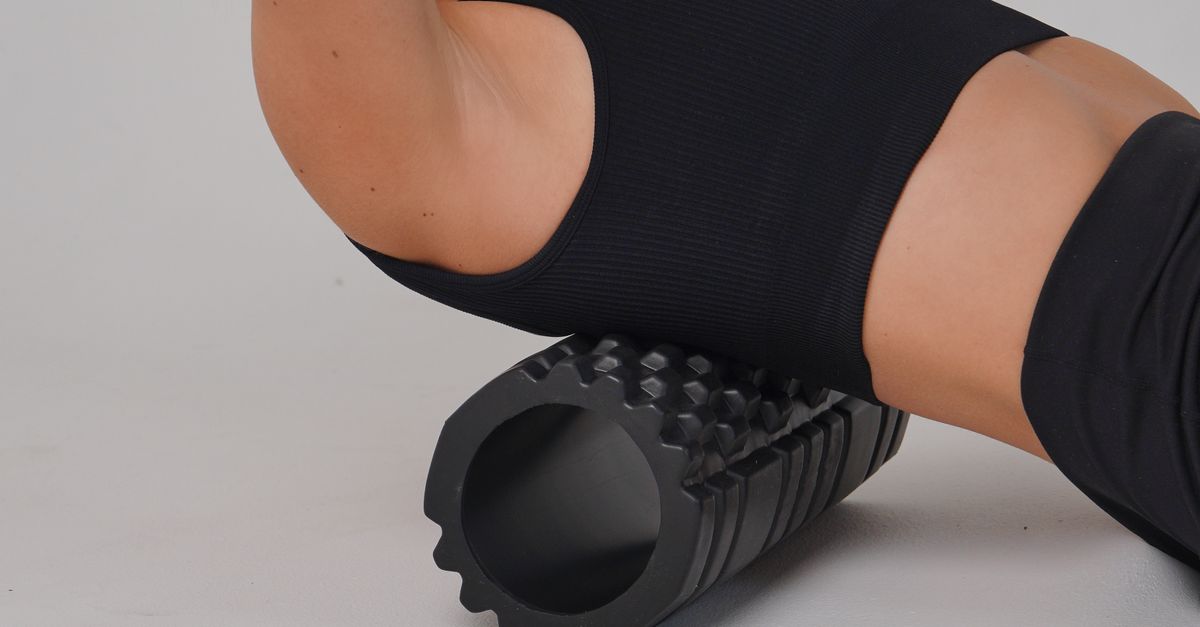 Adult woman practicing workout therapy with a foam roller on a white background.