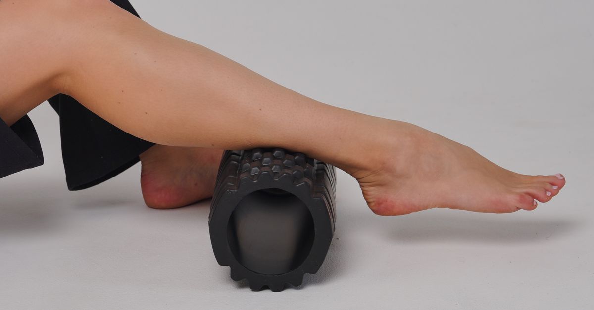 Close-up of a leg using a foam roller for stretching and muscle relief in a studio setting.