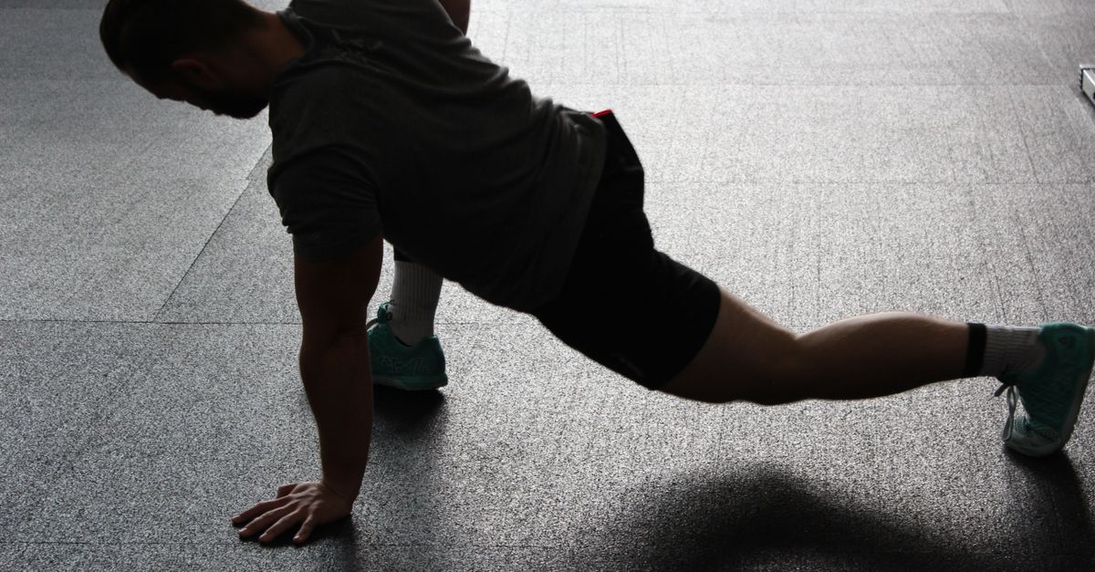 Silhouette of a man executing a stretching routine in a dim gym environment.