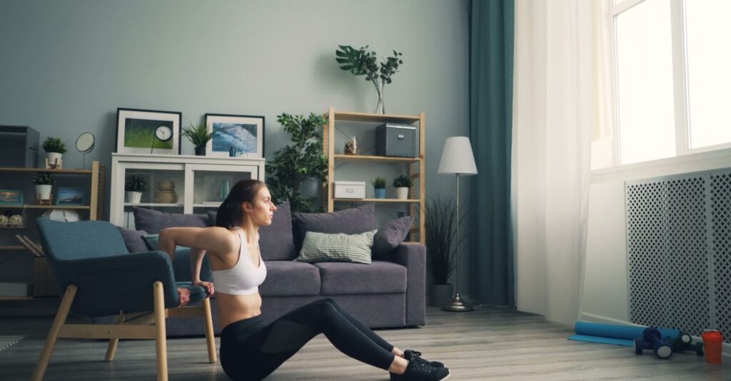 Woman doing tricep dips at home using a chair for support, promoting fitness indoors.