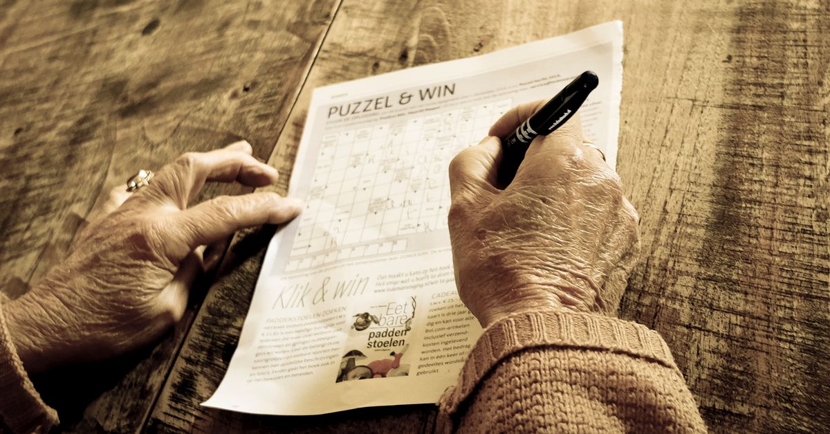 Close-up of a senior adult solving a puzzle on a rustic wooden table with a pen.
