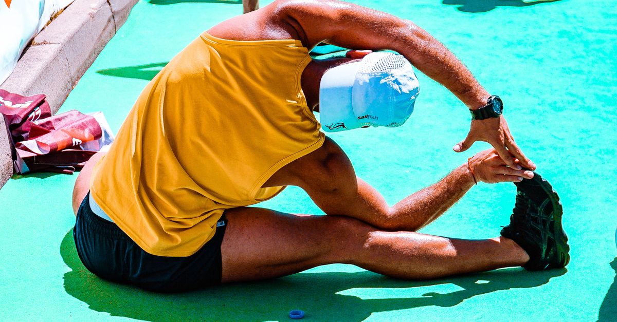 Athletic man stretches on a vibrant outdoor sports court, focusing on flexibility and fitness.