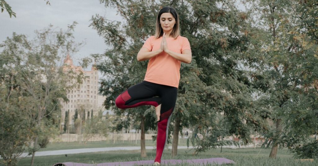 A woman in yoga pose outdoors on a mat in a park, showcasing balance and mindfulness.
