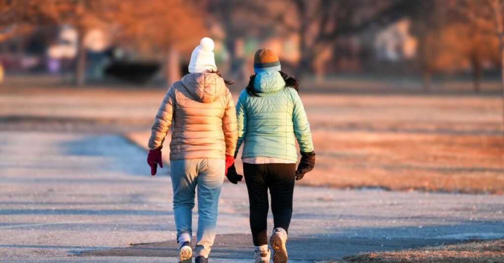 Two friends walking side by side in a winter park during sunset.