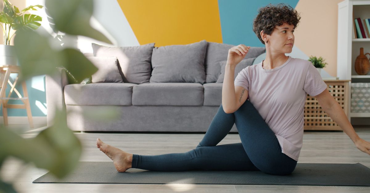 Woman doing yoga pose on mat in a stylish, modern living room with indoor plants.