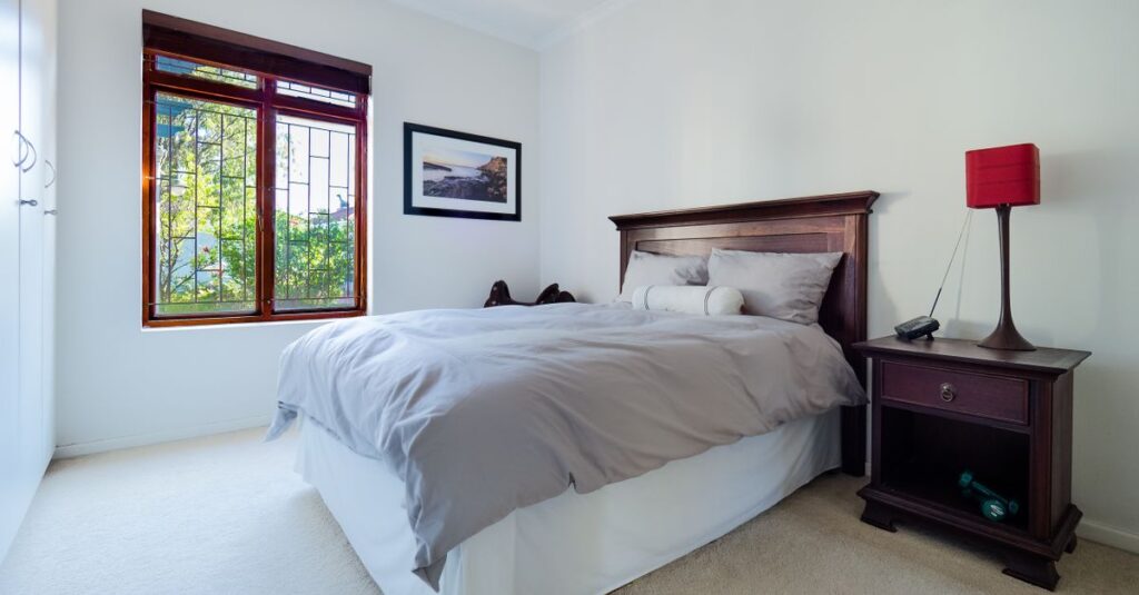 A stylish and comfortable bedroom interior featuring a wooden bed and nightstand with a red lamp and large window.