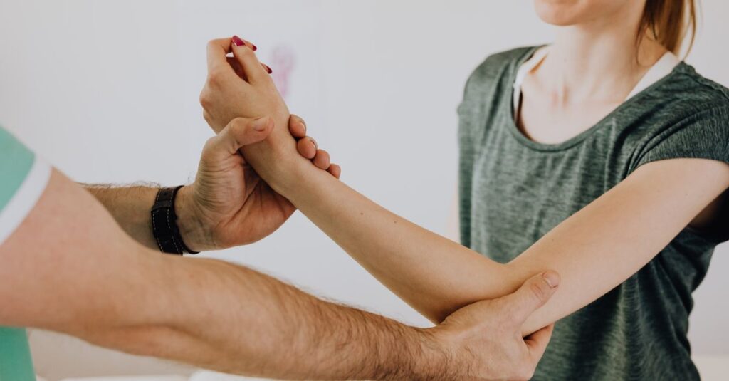 Crop faceless orthopedist in uniform and wristwatch checking up arm joint of slim woman in casual wear in doctor office in clinic