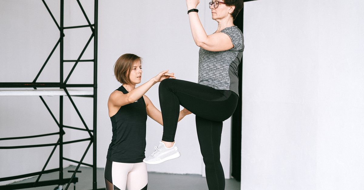 An elderly woman performs exercises with a fitness coach, focusing on a healthy lifestyle and wellness indoors.