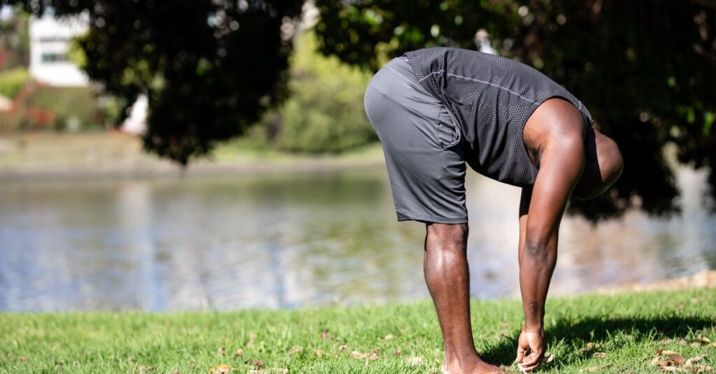 Athletic man in a park stretching near a lake during summer. Promotes fitness and relaxation.