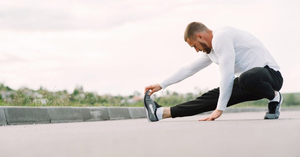 Adult male stretching outdoors, focusing on fitness and healthy lifestyle in a casual sportswear outfit.