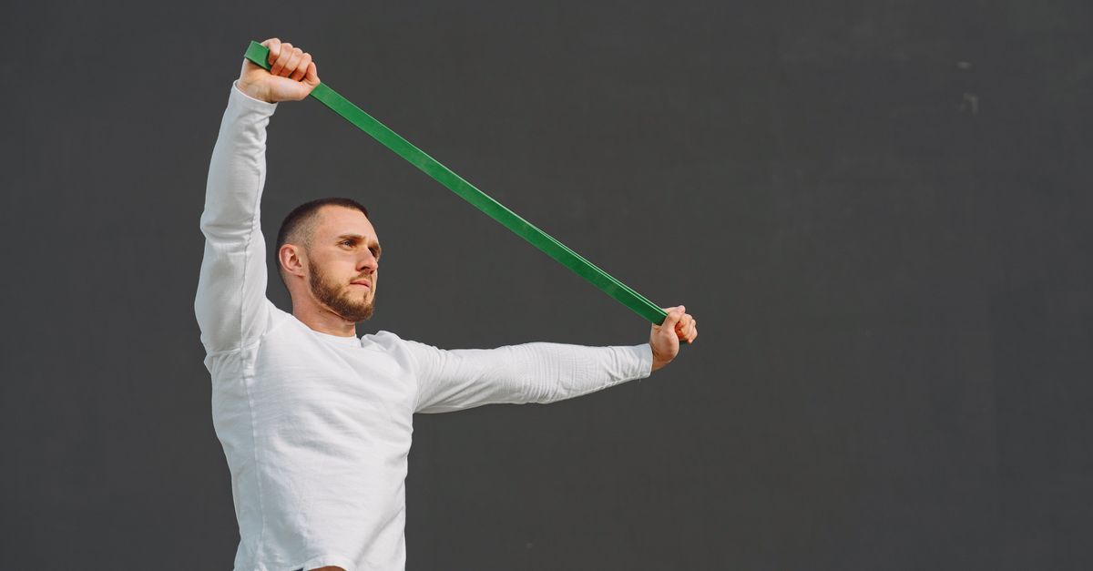 A man exercises with a resistance band against a plain background, promoting fitness.