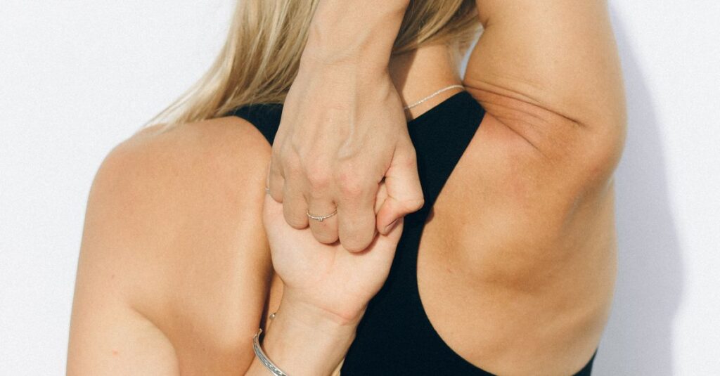 Back view of a woman in activewear stretching her arms outdoors against a white wall.