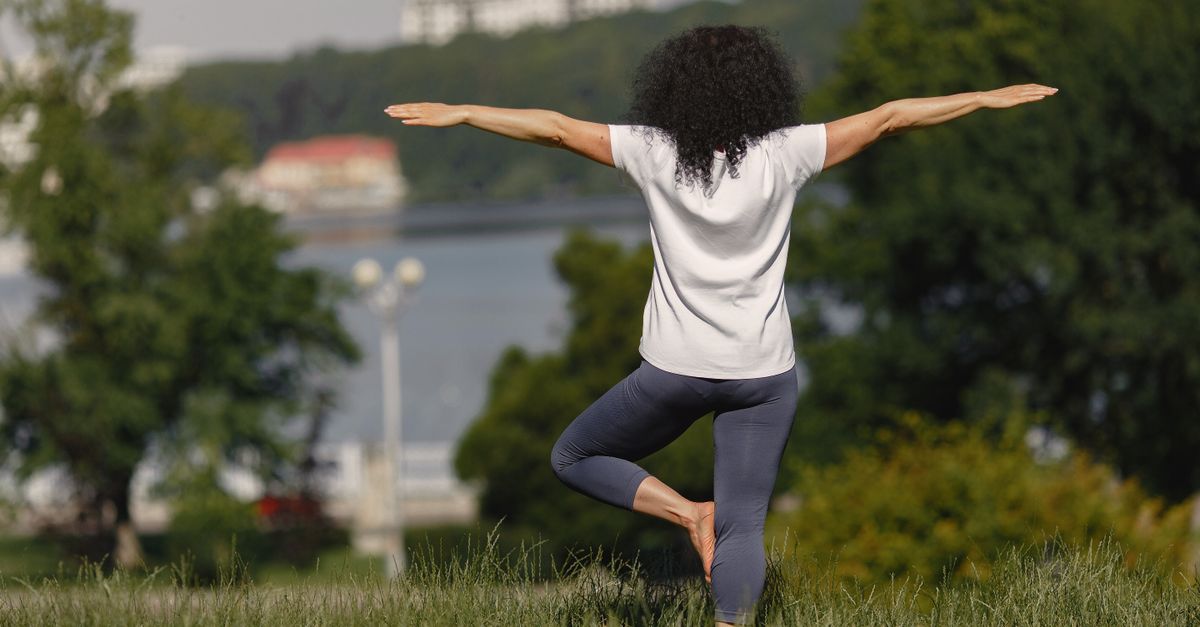 Woman performing yoga in a scenic park setting with lake and trees.