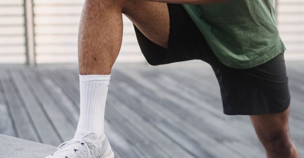 Adult man in green t-shirt stretching on a wooden deck outdoors, preparing for exercise.