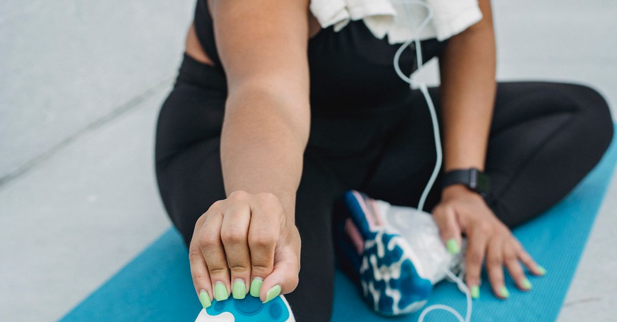 Woman enjoying a post-yoga exercise stretch on a mat while listening to music outdoors.