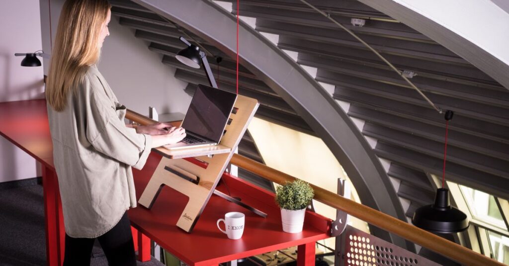 Woman using a laptop on a standing desk indoors in a creative workspace.