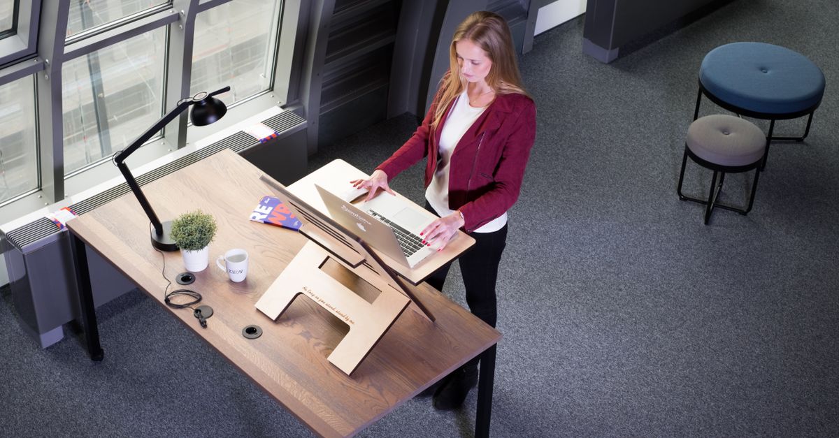A woman working on a laptop at a standing desk in a modern office setting.