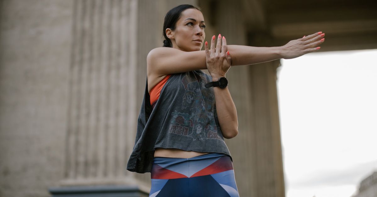 Athletic woman stretching her arms outdoors against a classic architectural backdrop.