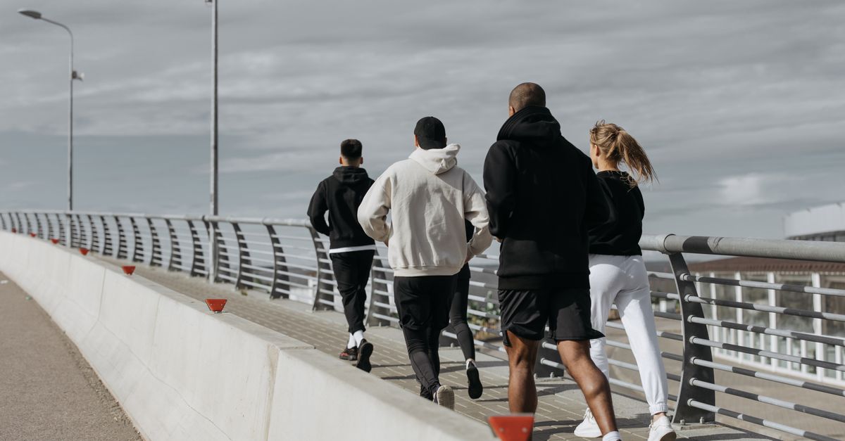 A diverse group of adults jogging together on a city bridge during the day.
