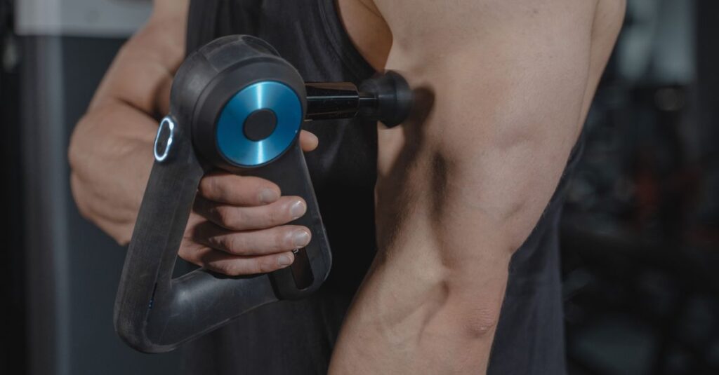 Close-up of a man using a massage gun for muscle relaxation on his arm.