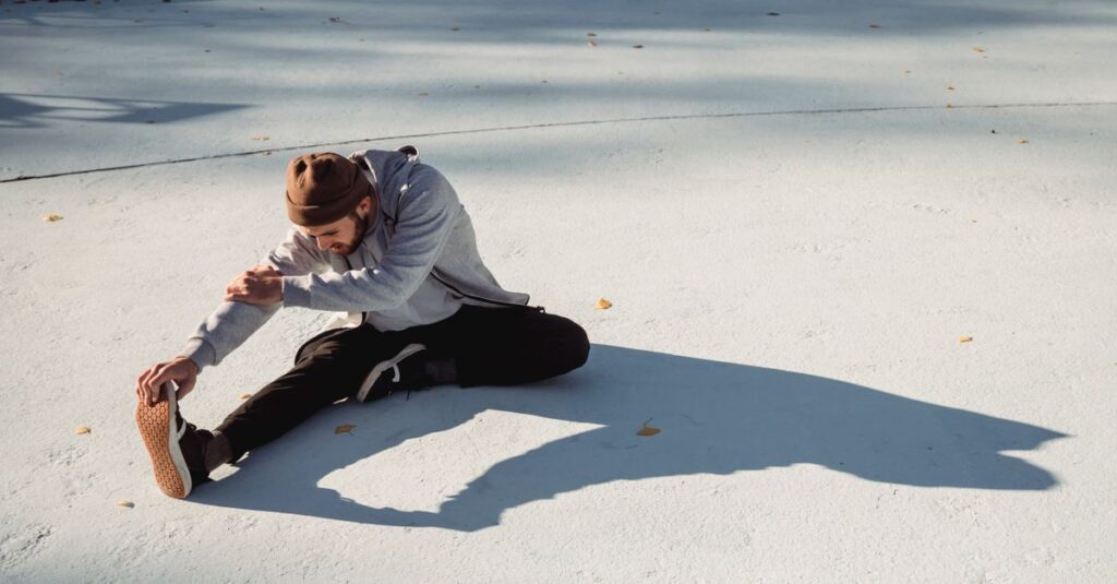 Attentive slender sportsman in casual clothes leaning forward while working out on urban pavement with shadow in sunlight