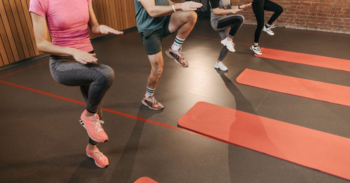 A group performs high knees together in an indoor fitness studio with yoga mats.