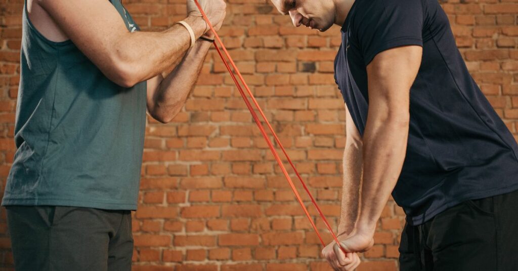 Two men exercising with a resistance band in a brick-walled gym setting.