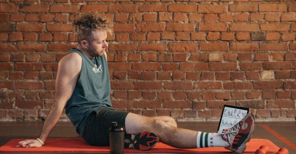 Athletic man sitting and resting on a mat in an urban gym, with a tablet and weights visible.
