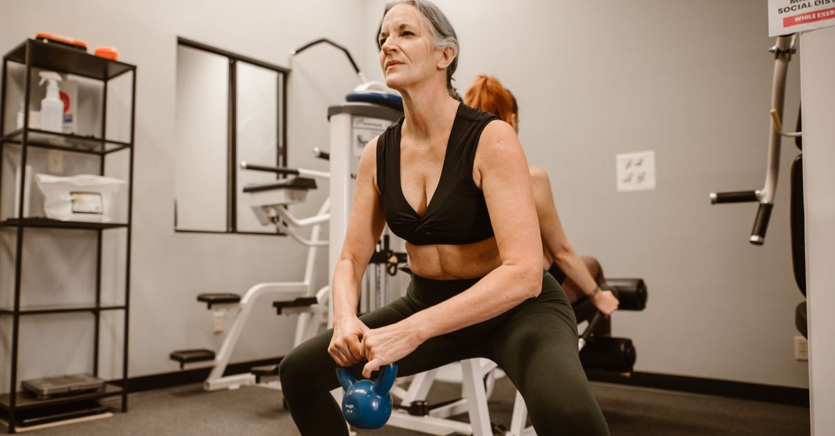 Active senior woman performing kettlebell squats for strength training at indoor gym.