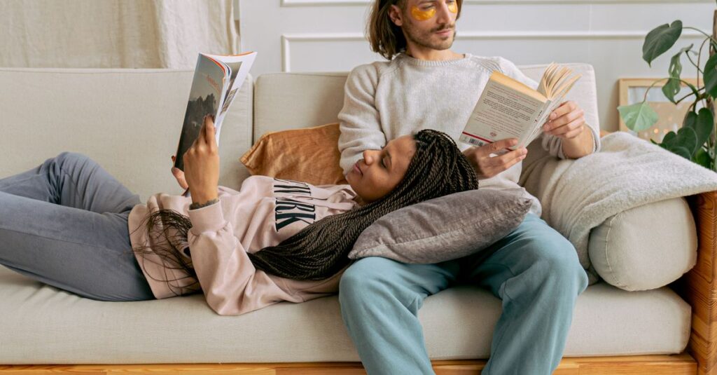 A couple lounges on a sofa enjoying a comfortable afternoon reading session.