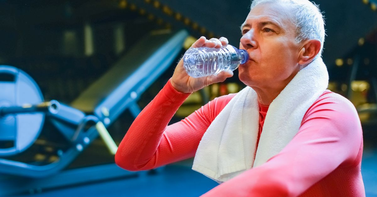Senior man in gym resting and drinking water post workout for hydration.