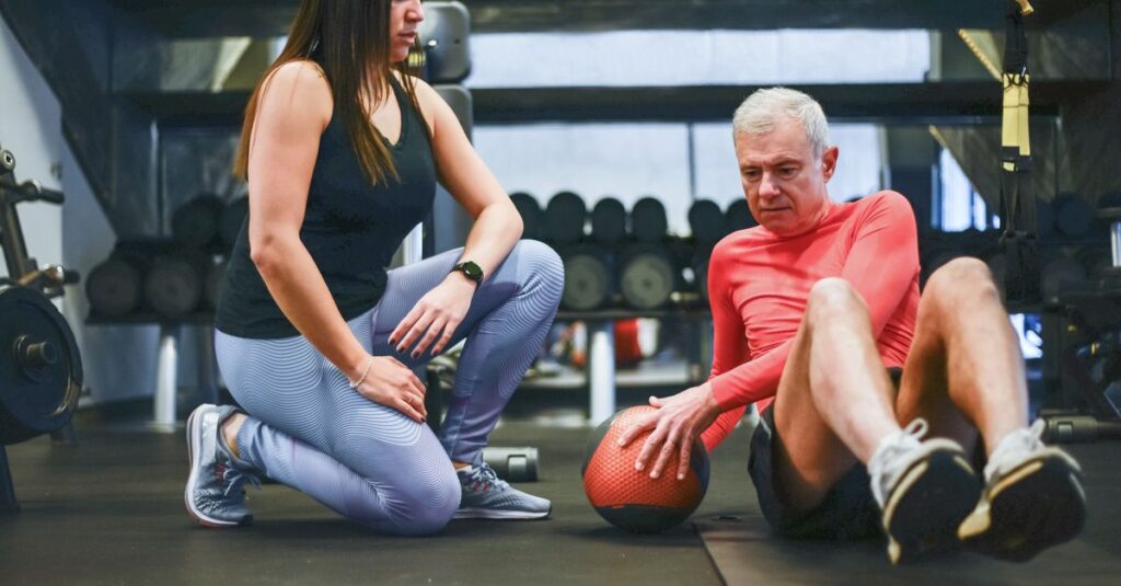 A senior man exercising with a personal trainer in a gym, focusing on core workouts.