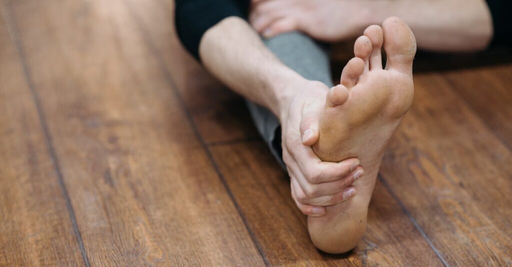 Close-up of a person doing a stretching exercise on a wooden floor, focusing on their bare foot.