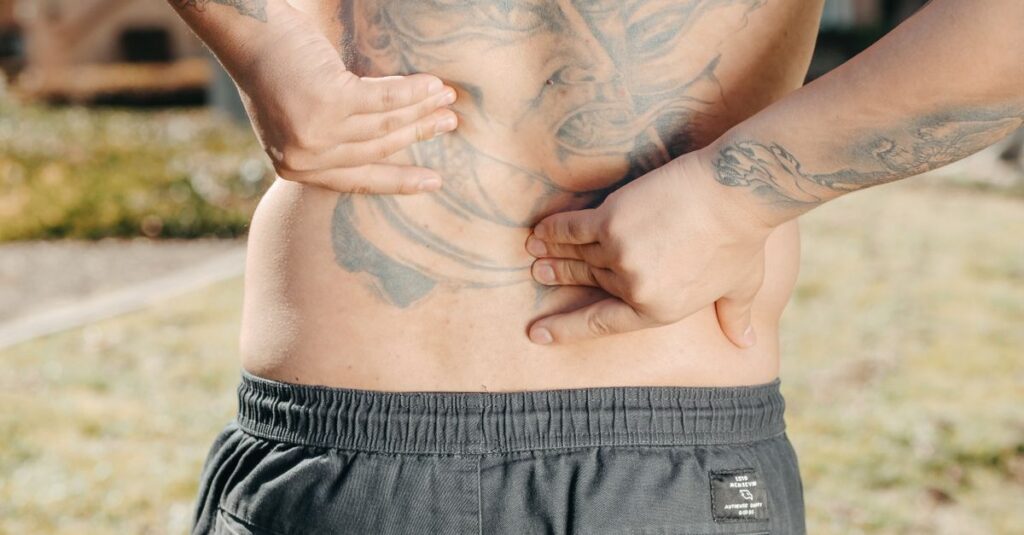 Close-up of a man holding his tattooed back outdoors, possibly experiencing back pain.
