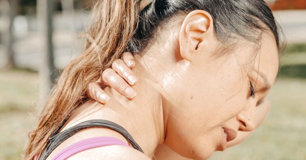 Close-up of a woman holding her neck, showing discomfort and pain outdoors.