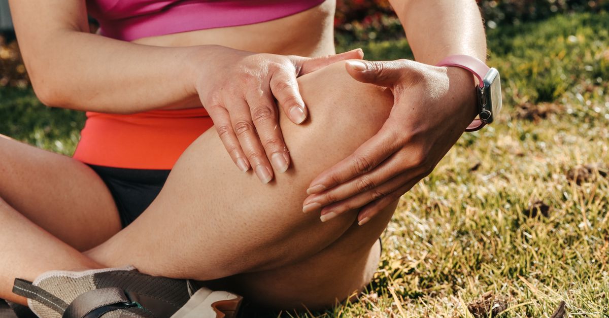Close-up of a woman sitting cross-legged on grass, holding her knee, wearing a smartwatch.
