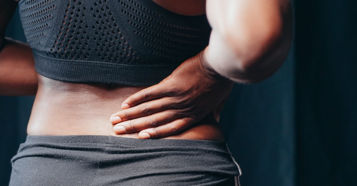 An adult of African descent holding their lower back in pain, indicating discomfort or injury.