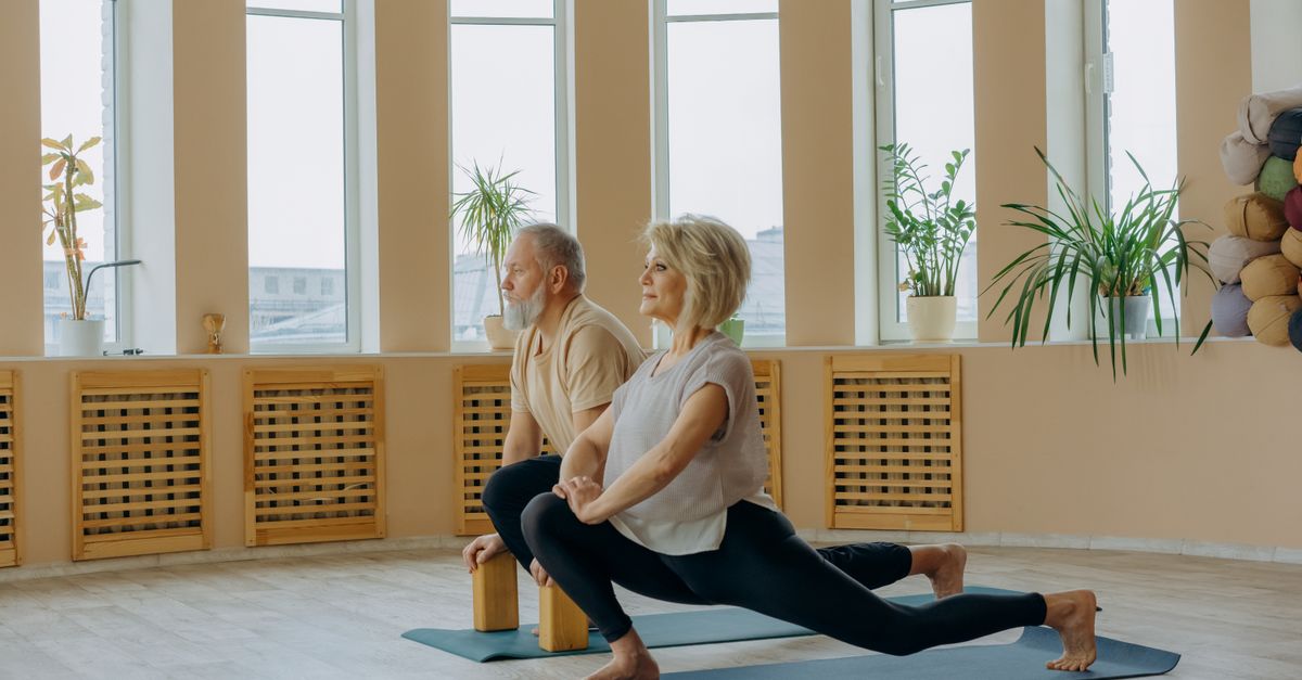 A senior couple practicing yoga indoors, focusing on a healthy lifestyle and flexibility.