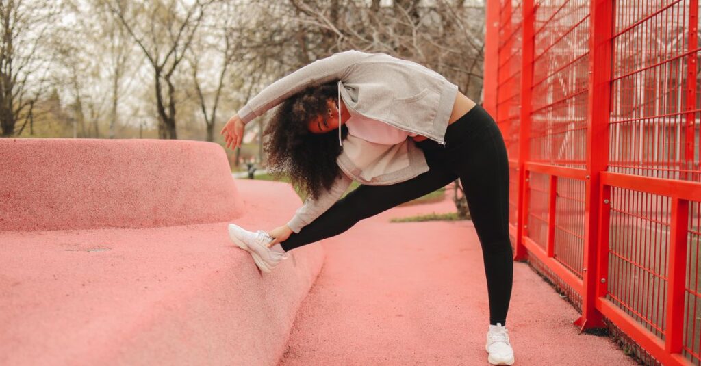Woman stretching outdoors against a bright red structure, promoting fitness and wellness.