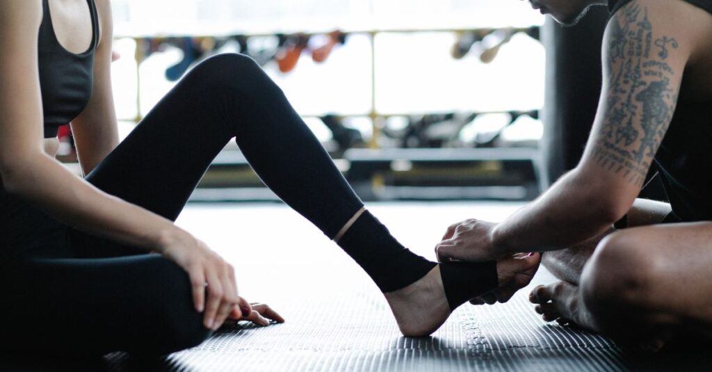 Two adults in gym attire preparing for a fitness session by wrapping an ankle.