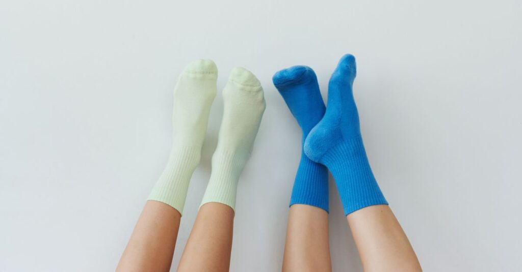 Two pairs of relaxed legs with pastel and vibrant socks on a clean white background.