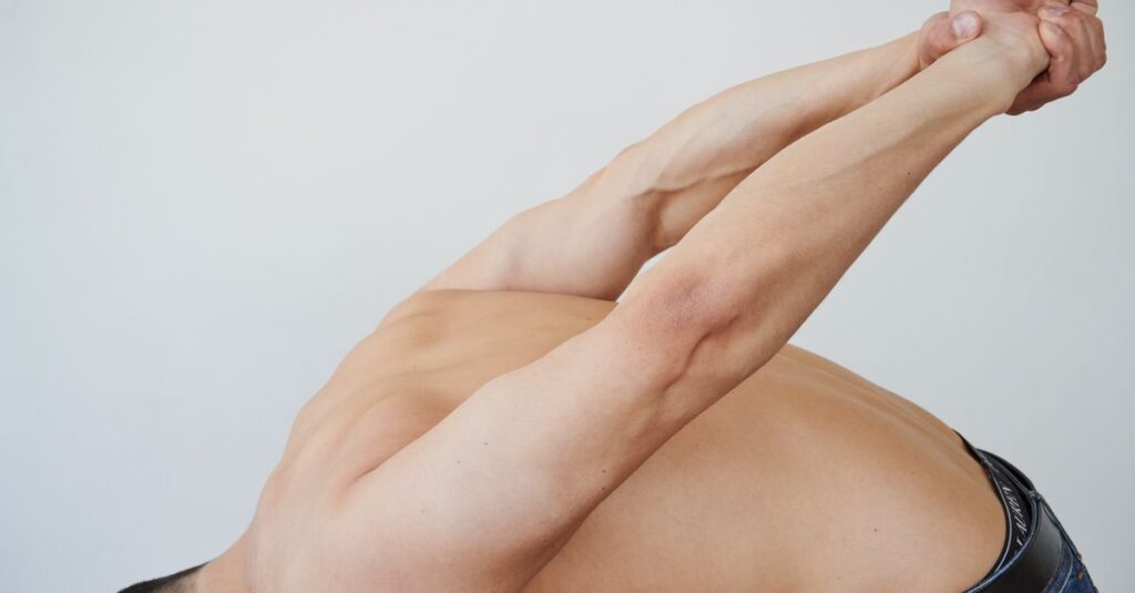 Close-up of a shirtless man stretching indoors, focusing on flexibility and muscle toning.